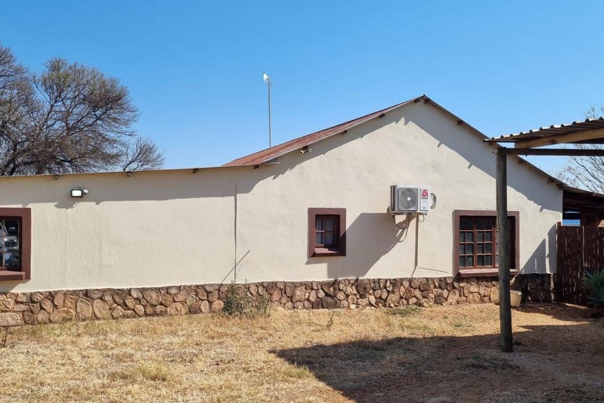 Rear exterior view of the house featuring a stone-clad base, timber-framed windows, and a corrugated metal roof with an installed air conditioning unit.