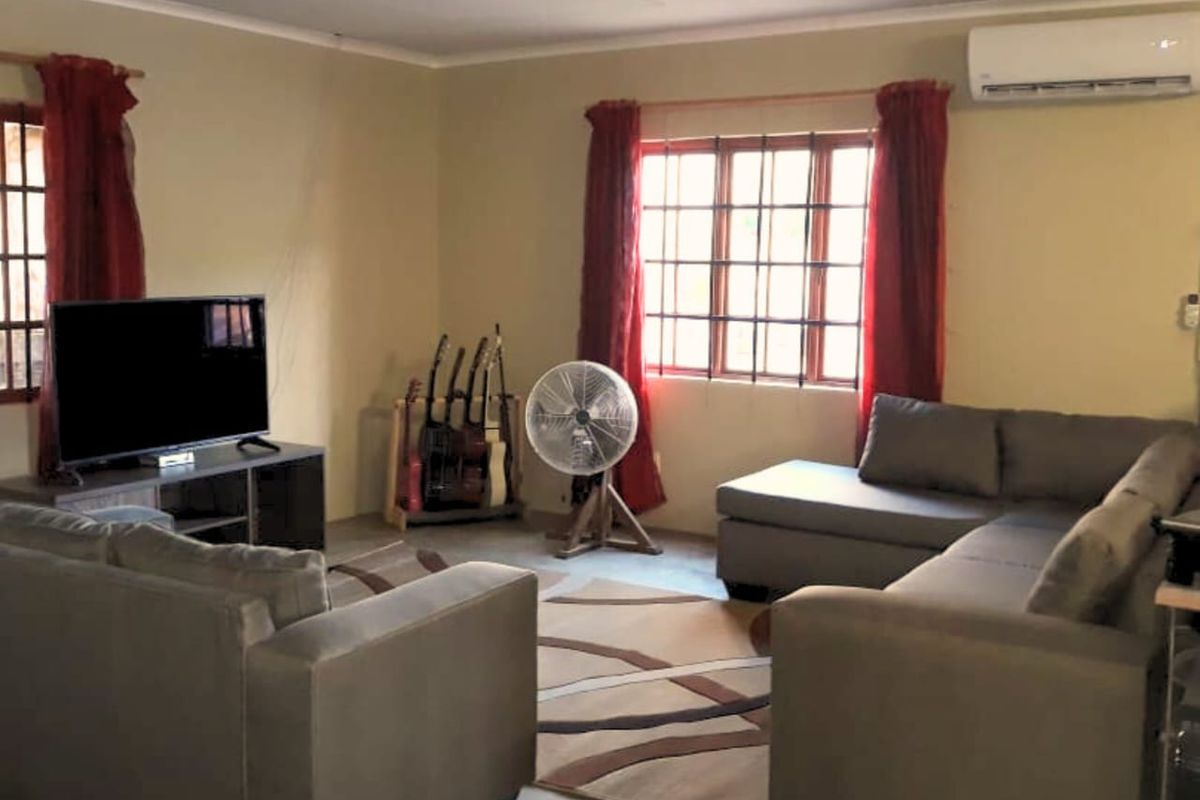 A comfortable living room featuring a wall-mounted air conditioning unit and security bars on the windows.