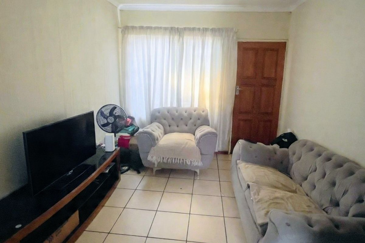 A compact living room featuring ceramic floor tiles, a timber door, and coved ceiling cornicing, providing a functional and neutral base for living space.