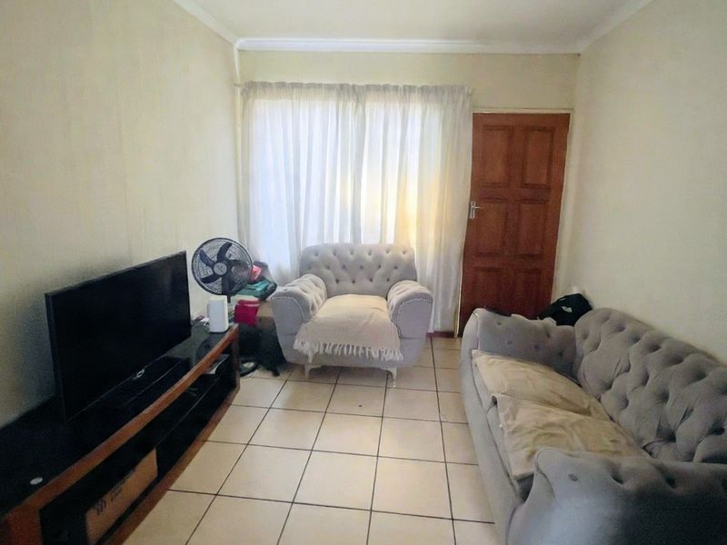 A compact living room featuring ceramic floor tiles, a timber door, and coved ceiling cornicing, providing a functional and neutral base for living space.