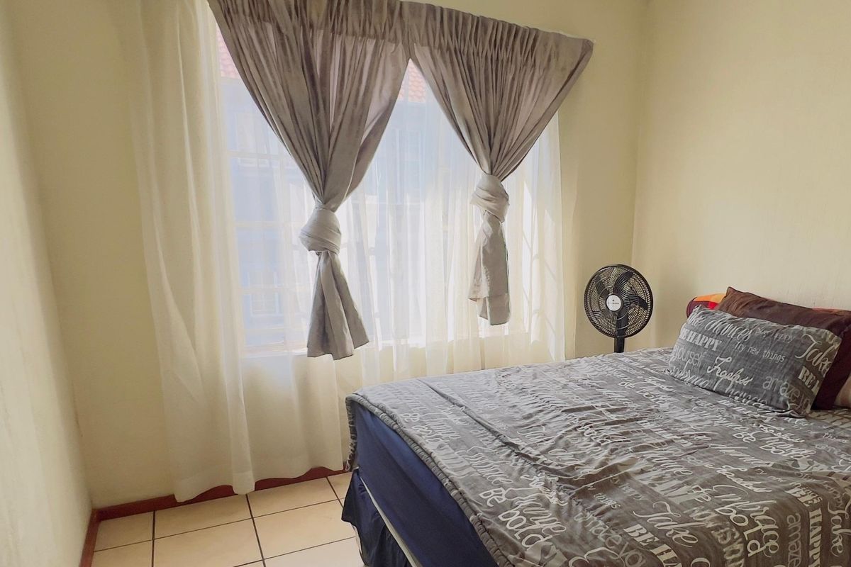 A bedroom featuring tiled flooring and a large window with curtain rails, providing natural light to the space.