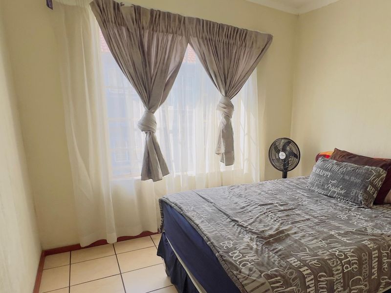 A bedroom featuring tiled flooring and a large window with curtain rails, providing natural light to the space.