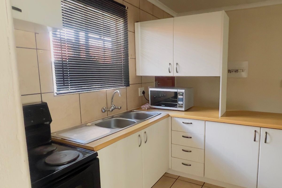 Functional kitchen featuring white cabinetry, laminate countertops, double stainless steel sink, and ceramic tiling throughout.
