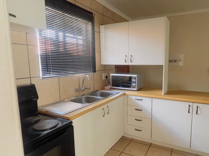 Functional kitchen featuring white cabinetry, laminate countertops, double stainless steel sink, and ceramic tiling throughout.