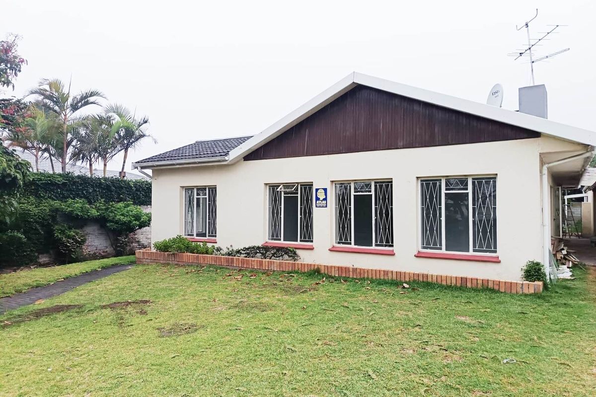 Rear view of the property featuring a lawn, brick planter box, and a single-story structure with tiled roof and security-fitted windows.
