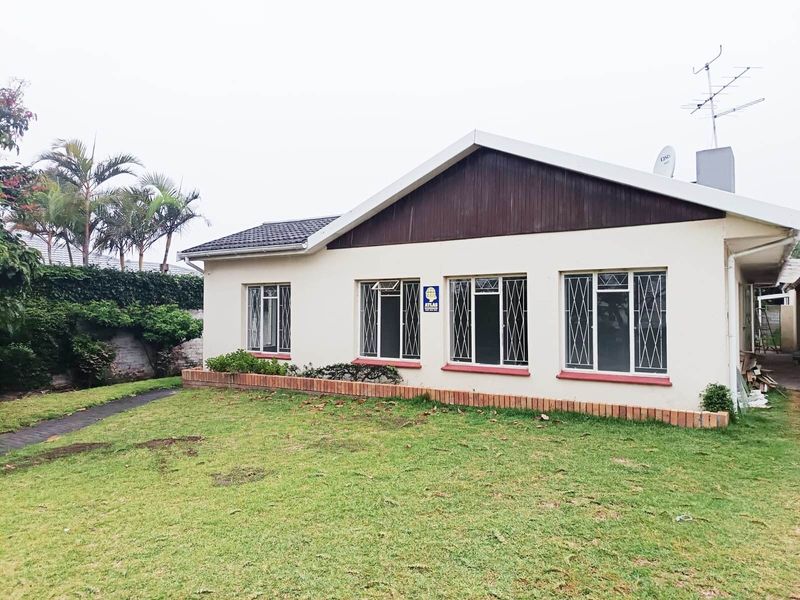 Rear view of the property featuring a lawn, brick planter box, and a single-story structure with tiled roof and security-fitted windows.