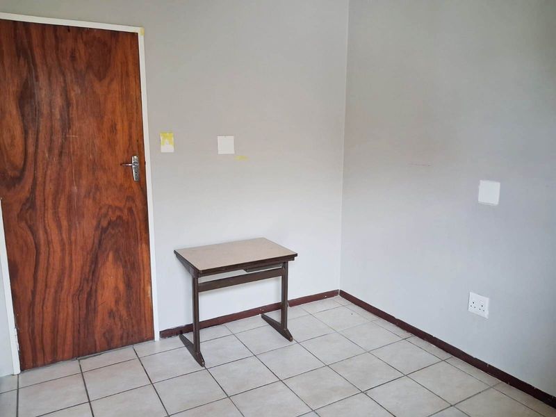 A vacant bedroom featuring tiled flooring, neutral walls, and a wooden door, offering a blank canvas for personalization.