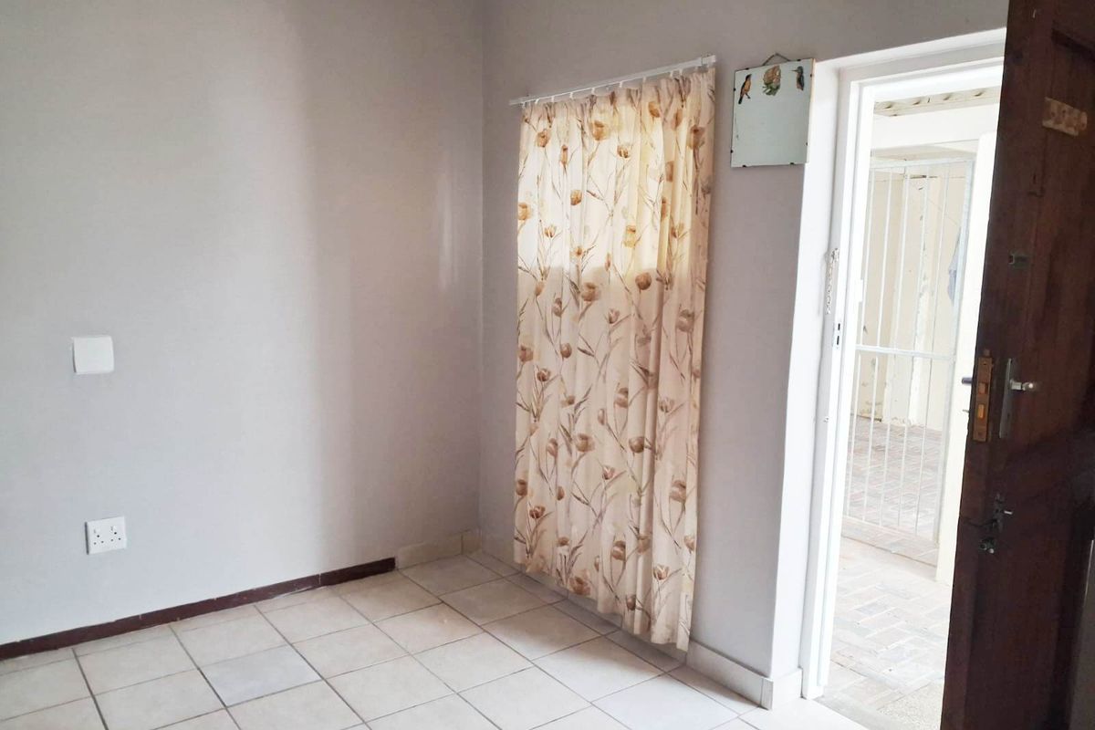 A clean, empty bedroom featuring neutral wall paint, tiled flooring, and direct access to an outdoor area through a wooden door.