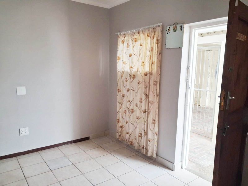 A clean, empty bedroom featuring neutral wall paint, tiled flooring, and direct access to an outdoor area through a wooden door.