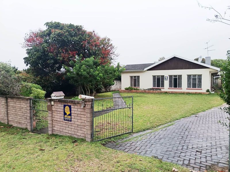 Front view of a single-story residential property featuring a paved driveway, gated entrance, and established garden area.