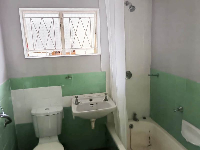 A functional bathroom featuring a bathtub with shower attachment, wall-mounted basin, and toilet, finished with dated green and white wall tiling.