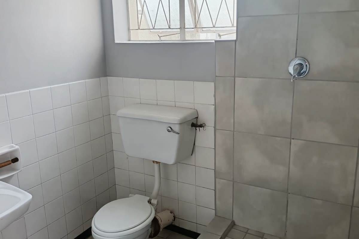 A functional bathroom featuring a tiled shower enclosure, standard toilet, and tiled finishes. The space is ready for modernization and cosmetic updates.