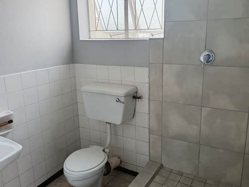 A functional bathroom featuring a tiled shower enclosure, standard toilet, and tiled finishes. The space is ready for modernization and cosmetic updates.