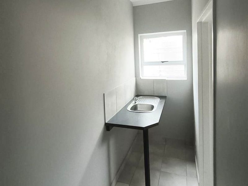 A compact, functional laundry area featuring a stainless steel sink, tiled splashback, and neutral tiled flooring, providing a clean and practical utility space.