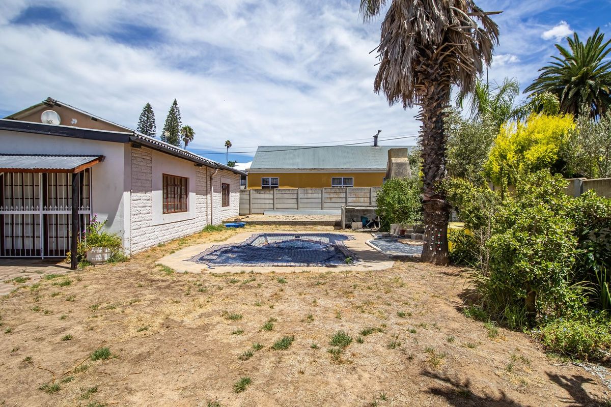 Rear garden area featuring a swimming pool with a cover, paved patio section, and established palm tree, set within a fenced residential backyard.