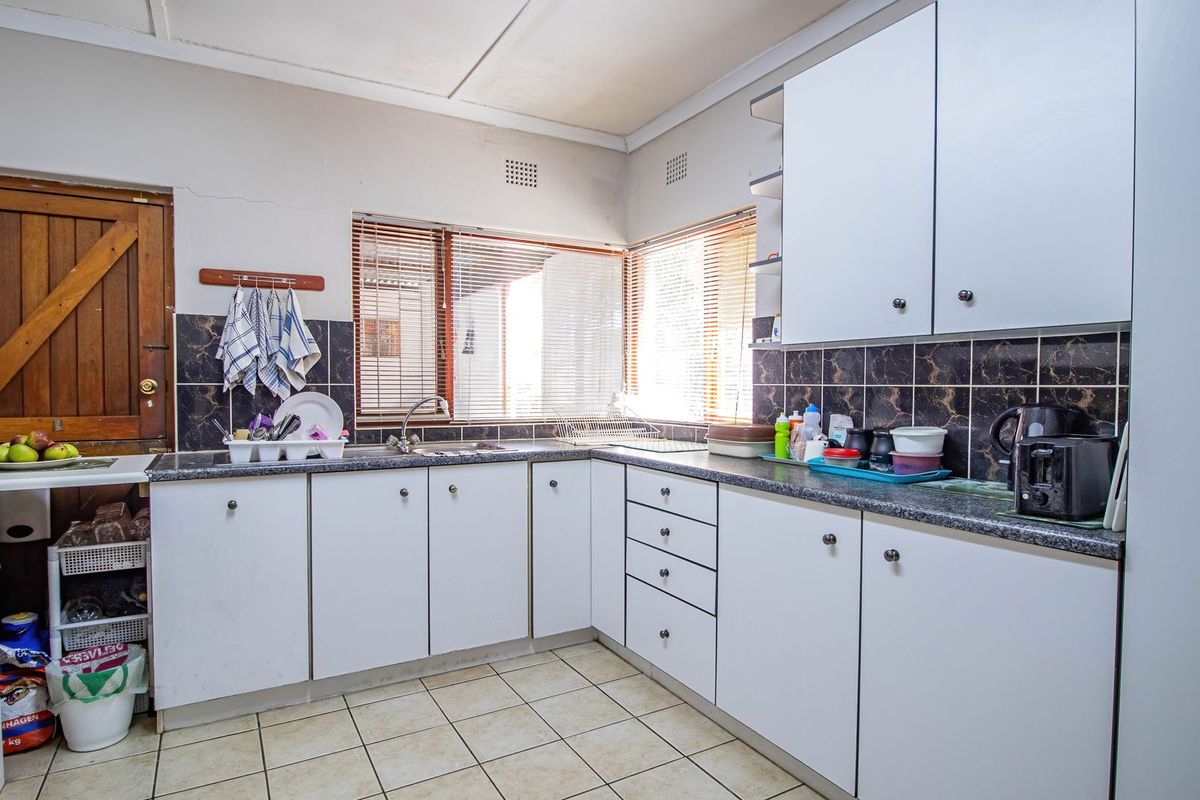 A functional kitchen featuring white cabinetry, dark granite-look countertops, tiled flooring, and a corner window layout with integrated oven and sink.