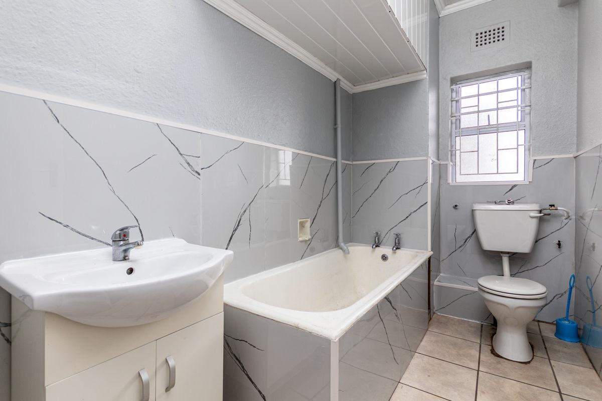 A functional bathroom featuring a bathtub, pedestal vanity with basin, and a standard toilet, finished with marble-look wall tiles and tiled flooring.