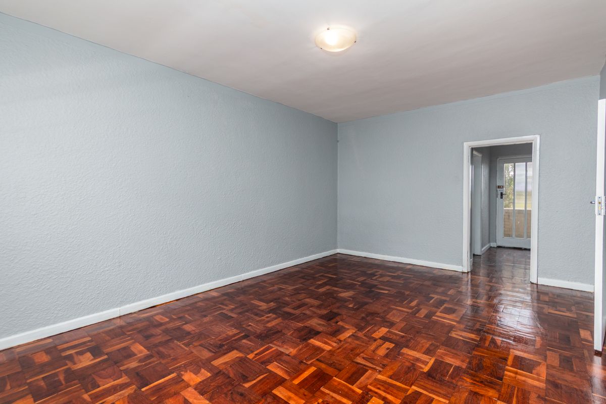 An empty living room featuring polished parquet flooring, light blue textured walls, and a doorway leading to an exterior balcony.