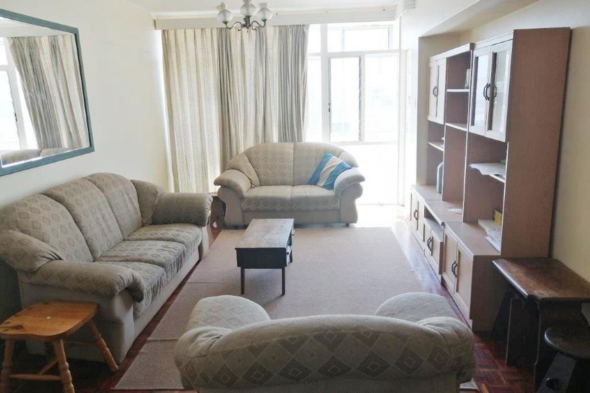 A living room featuring parquet flooring, large windows with curtains, and a built-in shelving unit.