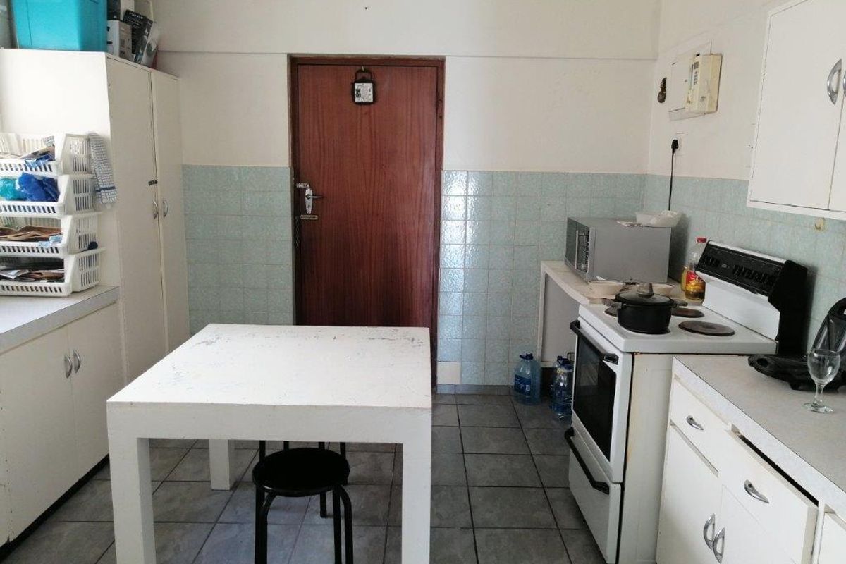 A dated kitchen featuring white cabinetry, tiled splashbacks, and a freestanding electric stove, offering a functional layout with potential for modernization.