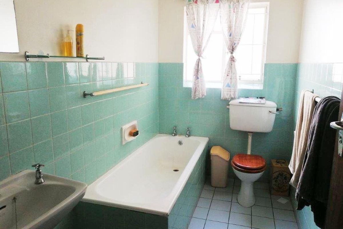 A dated bathroom featuring original light green wall tiles, a standard bathtub, a pedestal basin, and a low-level flush toilet.