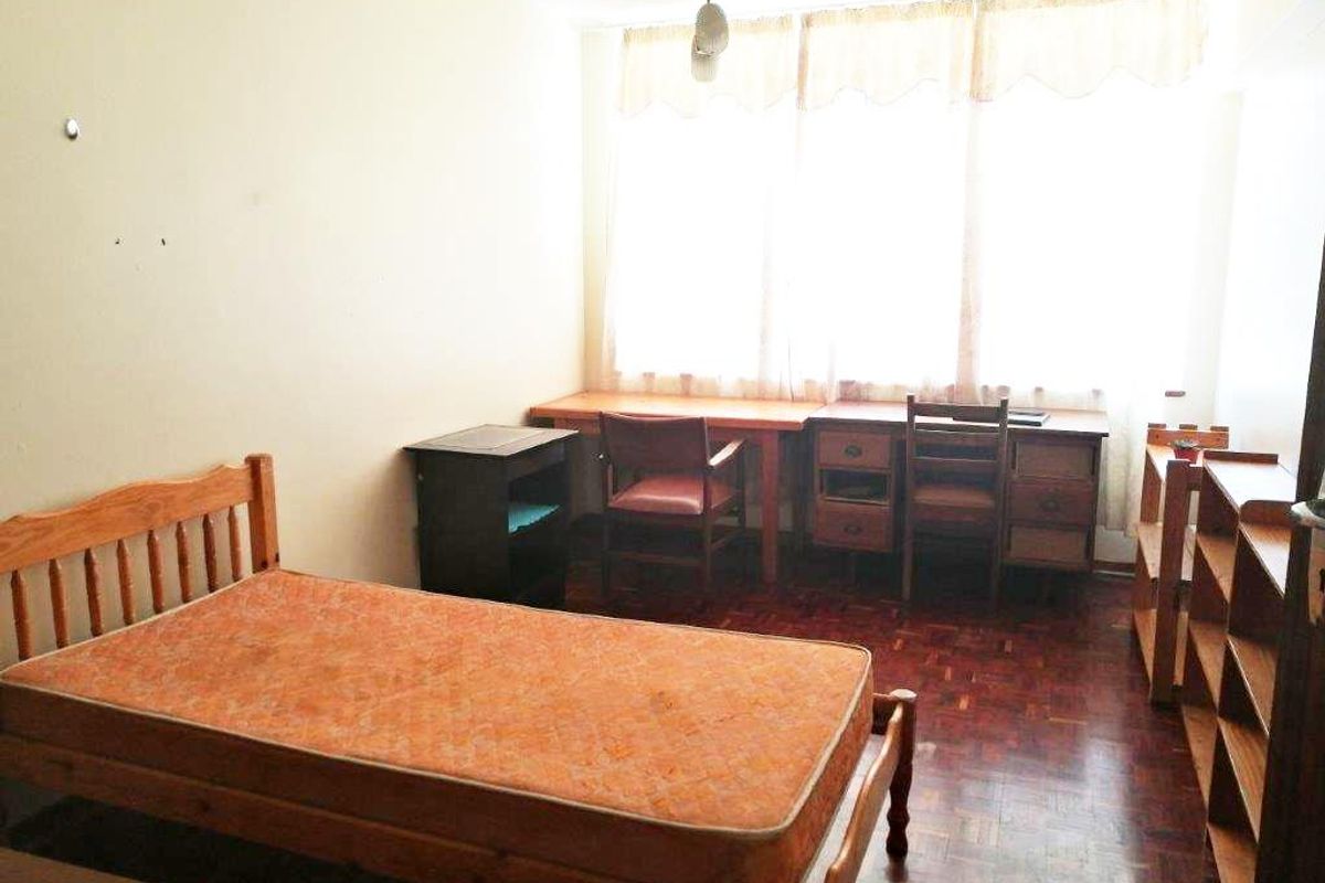 A bedroom featuring parquet flooring and a large window, providing a functional space with potential for modernization.