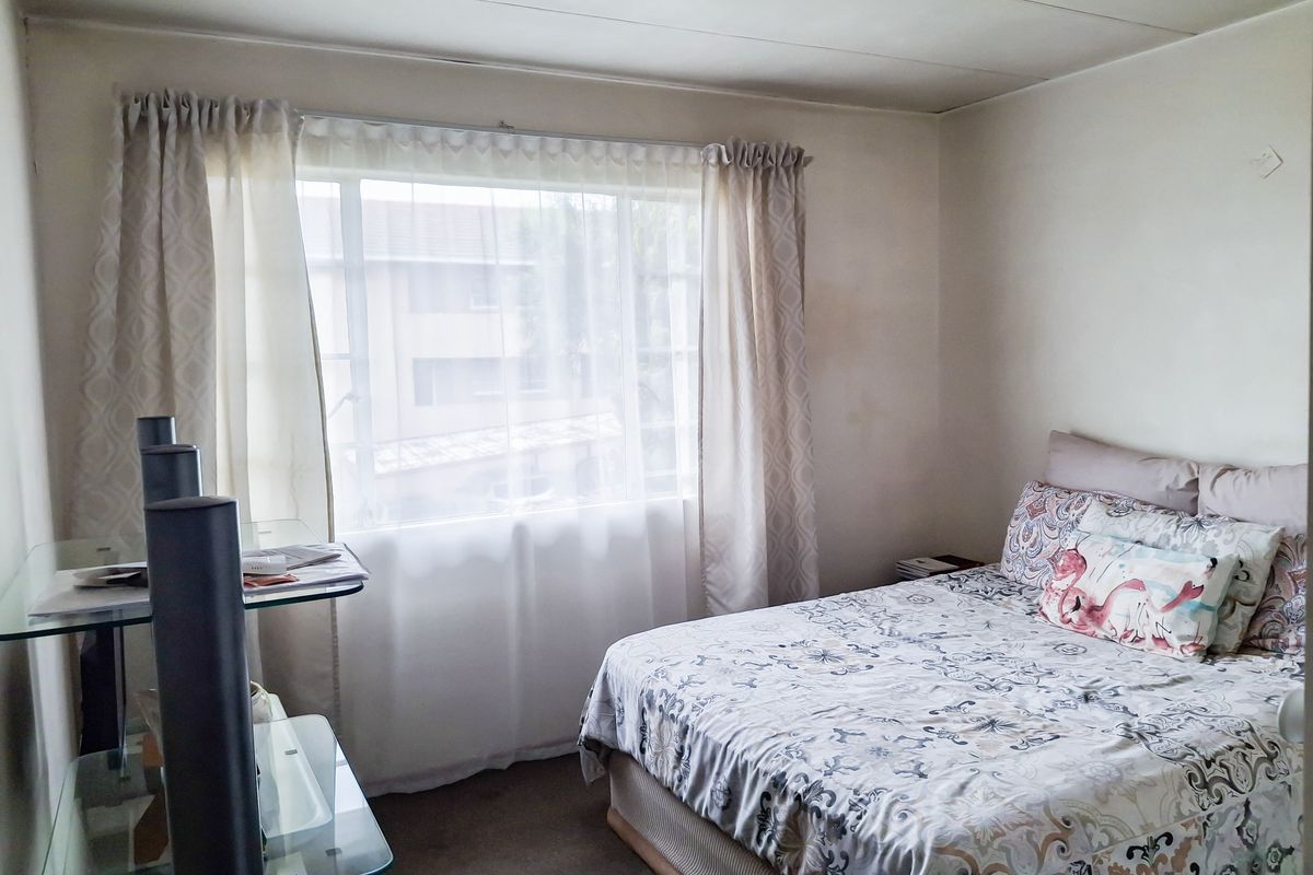 A functional bedroom featuring a large window with natural light, neutral wall finishes, and carpeted flooring.