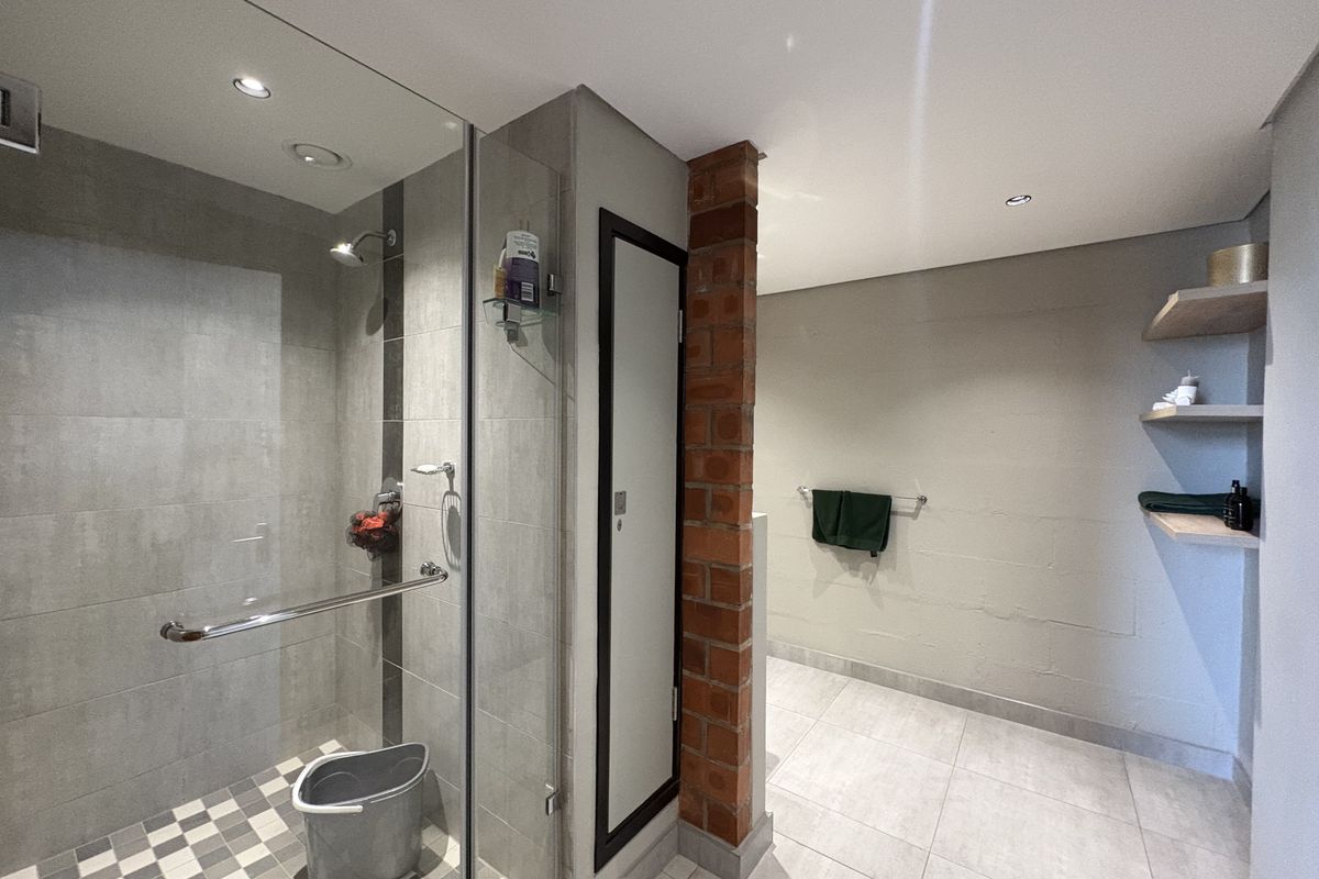 Modern bathroom featuring a walk-in glass shower with grey tiling, exposed brick column detail, and built-in floating timber shelving.