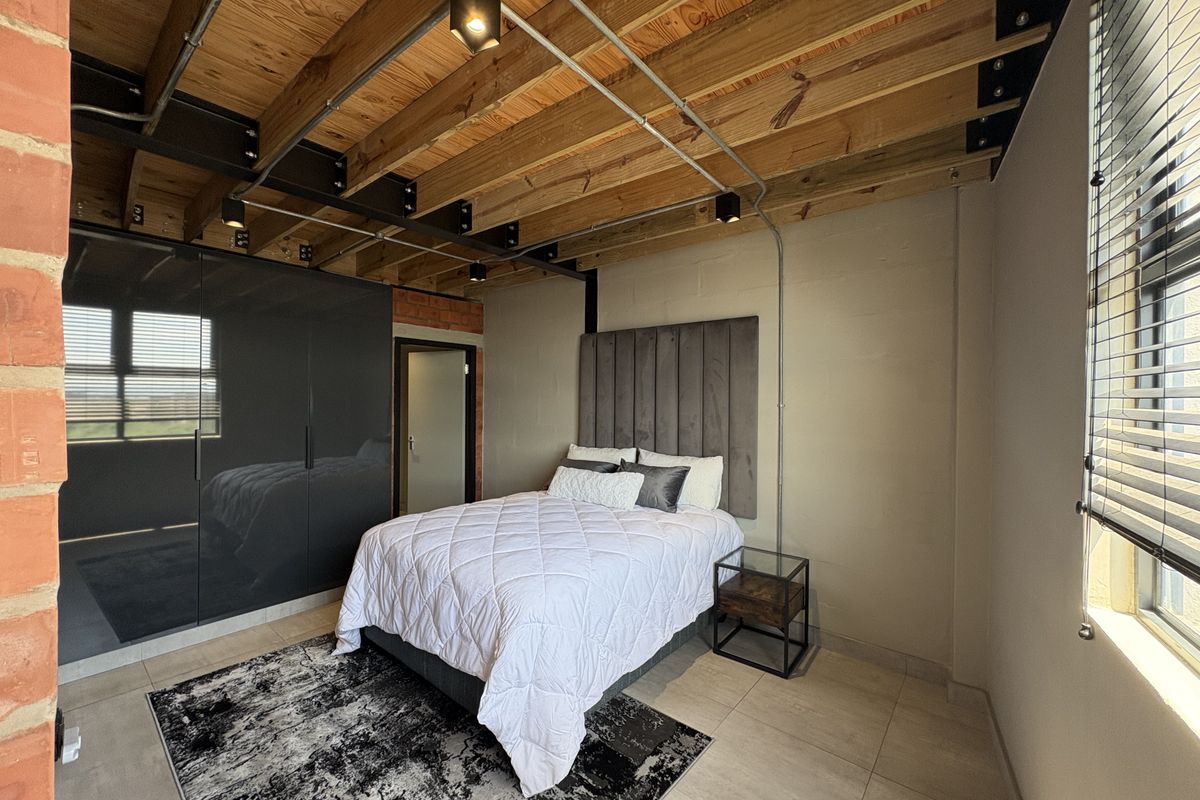 Industrial-style bedroom featuring exposed timber ceiling beams, brickwork accents, tiled flooring, and built-in floor-to-ceiling cabinetry.