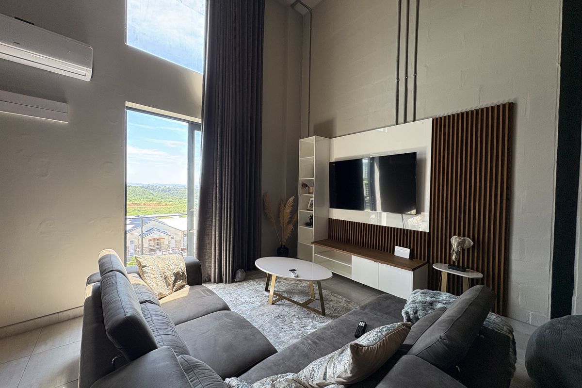 Spacious living room featuring double-volume ceilings, large floor-to-ceiling windows with scenic views, and a modern built-in media wall with timber slat detailing.