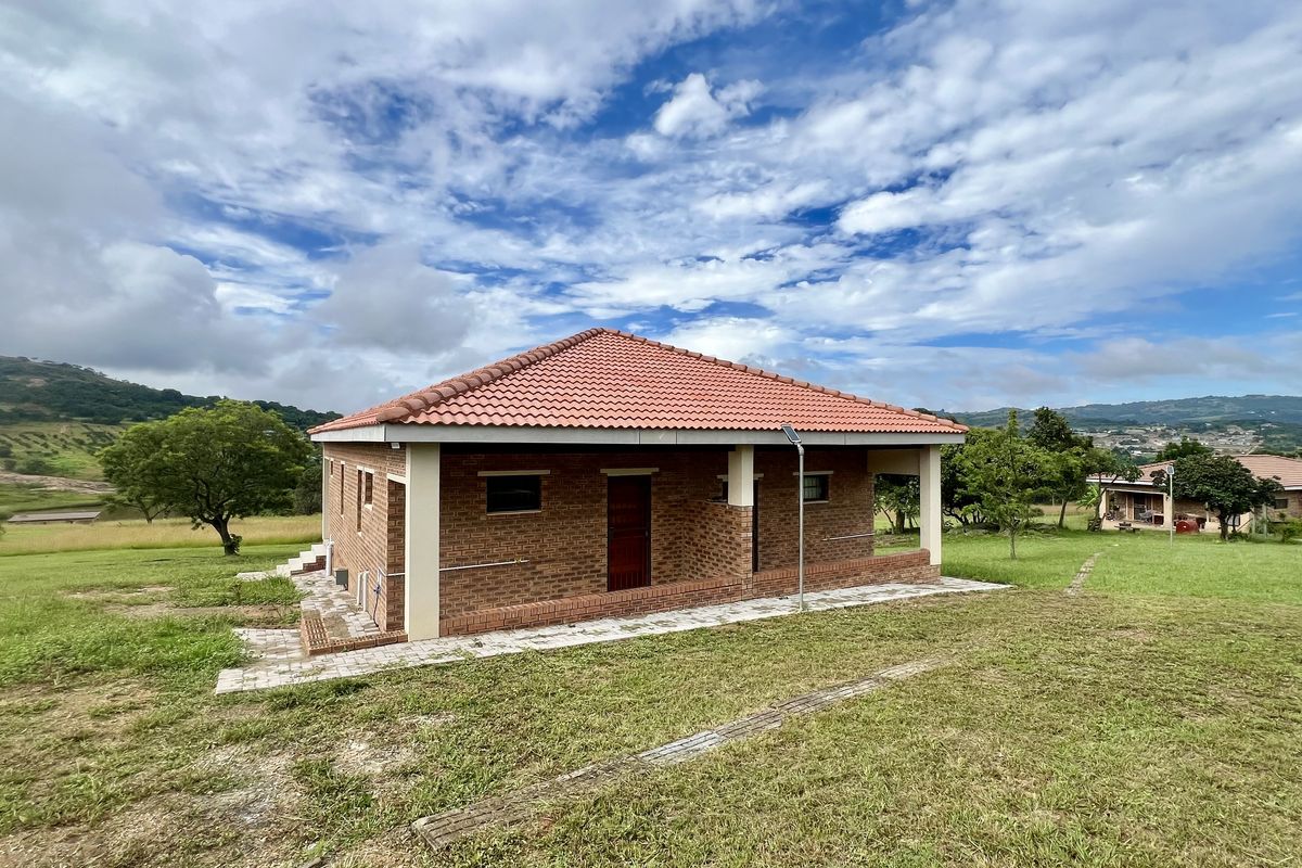 A view of the rear exterior of a brick-built property featuring a tiled roof and a covered patio area set within a spacious landscape.