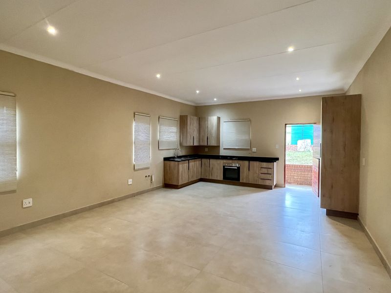 Spacious open-plan living and kitchen area featuring modern wood-finish cabinetry, integrated oven, tiled flooring, and recessed lighting with direct access to the exterior.