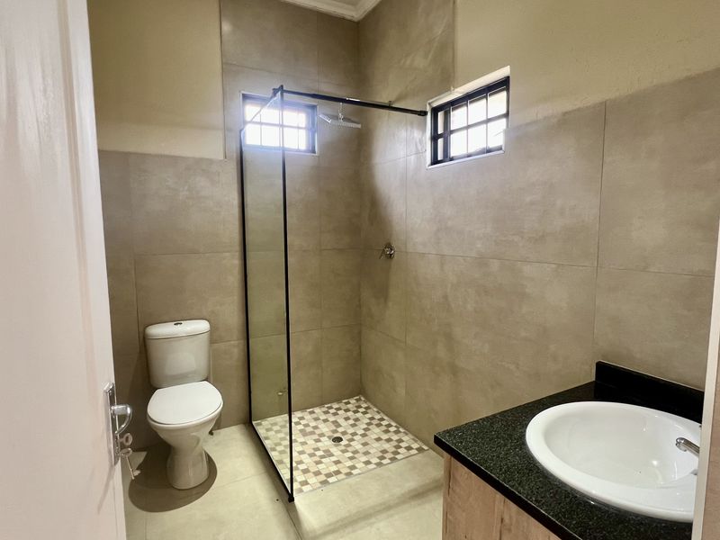 A modern bathroom featuring a walk-in shower with a glass screen, a vanity with a granite countertop, and neutral floor-to-ceiling wall tiles.