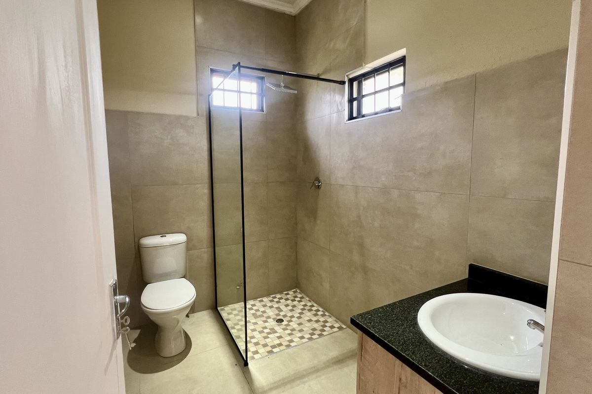 A modern bathroom featuring a walk-in shower with a glass screen, a vanity with a granite countertop, and neutral floor-to-ceiling wall tiles.