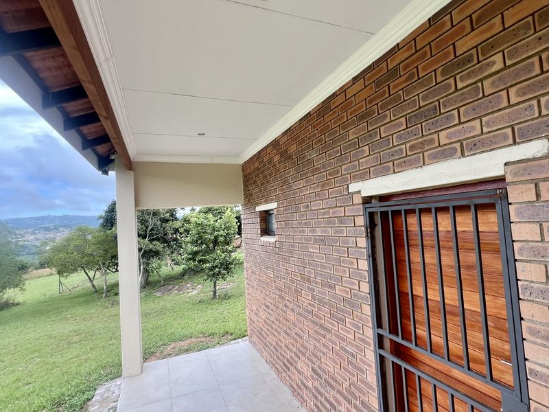 A covered patio area featuring exposed brickwork, tiled flooring, and a secure timber entrance door, overlooking a green landscape.