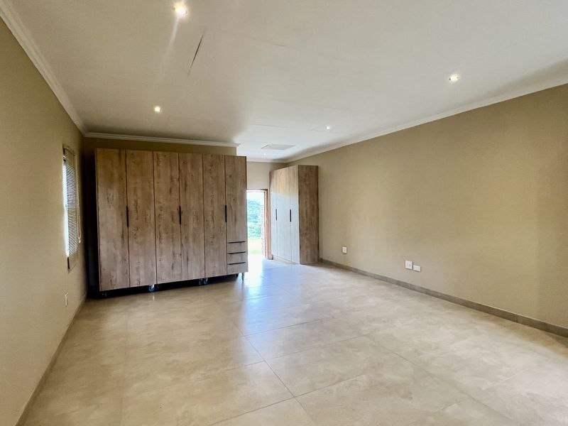 Spacious bedroom featuring neutral tiled flooring, recessed downlighting, and extensive built-in wooden cabinetry for ample storage.