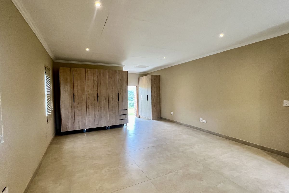 Spacious bedroom featuring neutral tiled flooring, recessed downlighting, and extensive built-in wooden cabinetry for ample storage.
