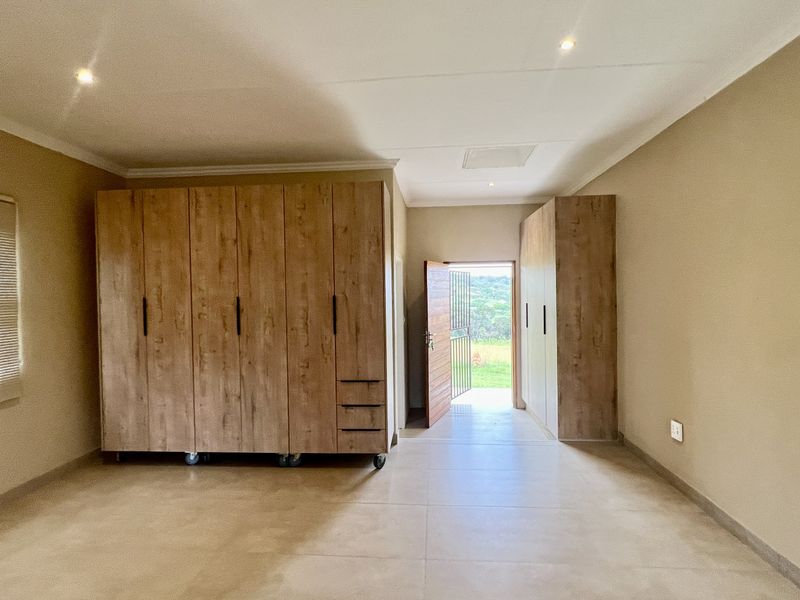 Spacious bedroom featuring neutral tiled flooring, recessed downlighting, and extensive built-in wooden cabinetry with direct access to an outdoor area.