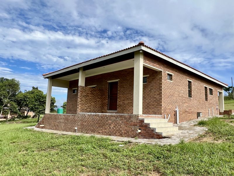 A modern face-brick residential building featuring a covered patio, tiled roof, and paved exterior walkway set within a spacious grassy landscape.