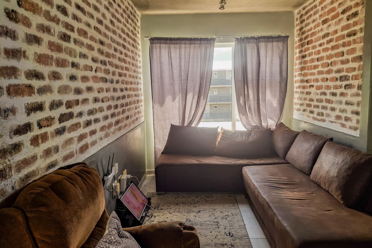 A living room featuring exposed brick feature walls, tiled flooring, and a window with curtains providing natural light.