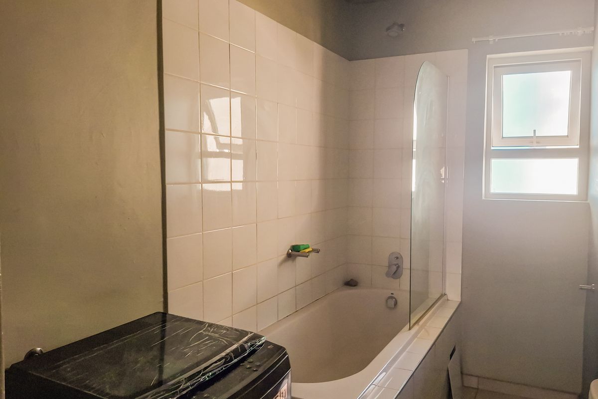 A functional bathroom featuring a built-in bathtub with a glass shower screen, tiled splashback, and a window for natural light.