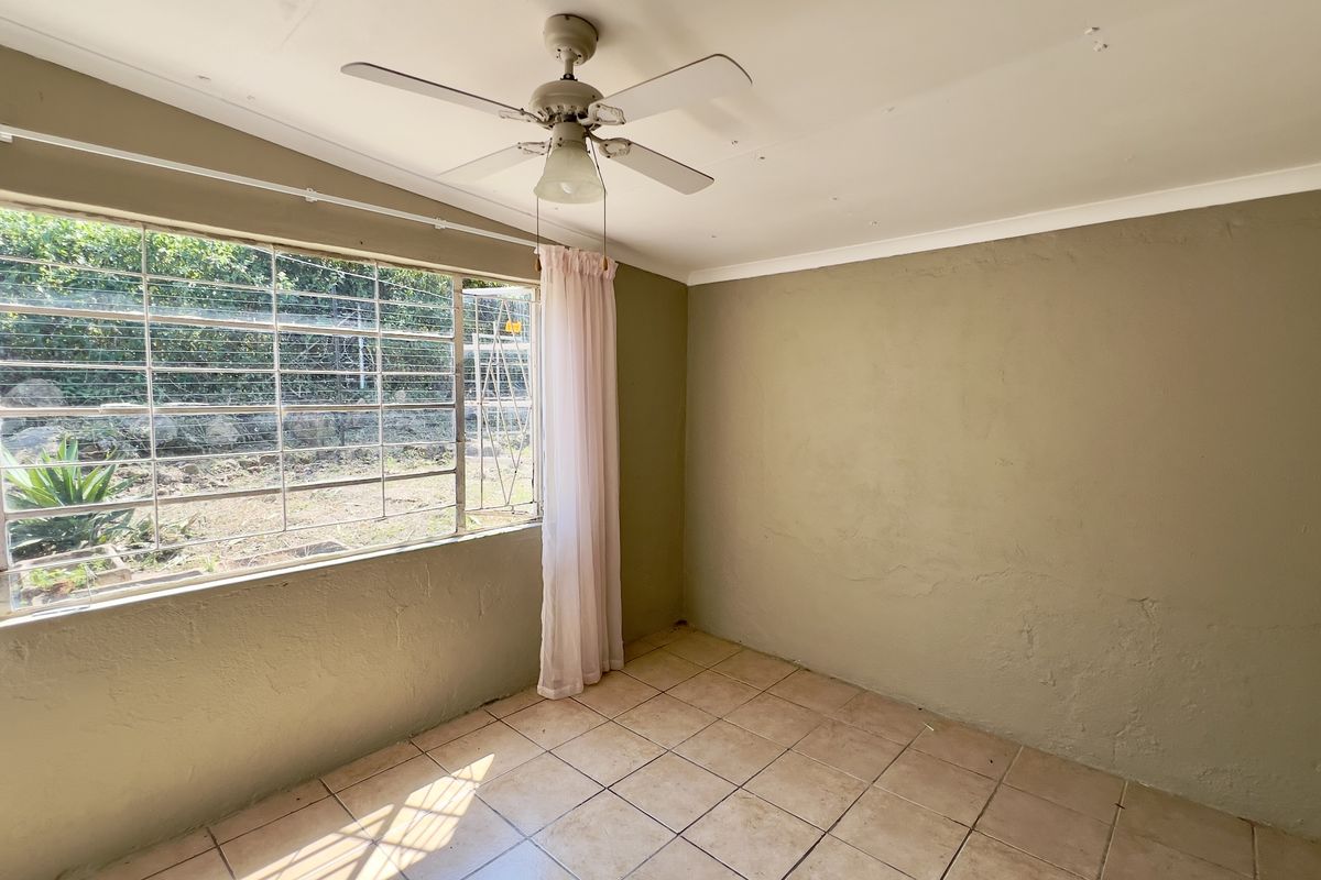 A vacant bedroom featuring tiled flooring, a ceiling fan, and large windows with security bars overlooking the garden.