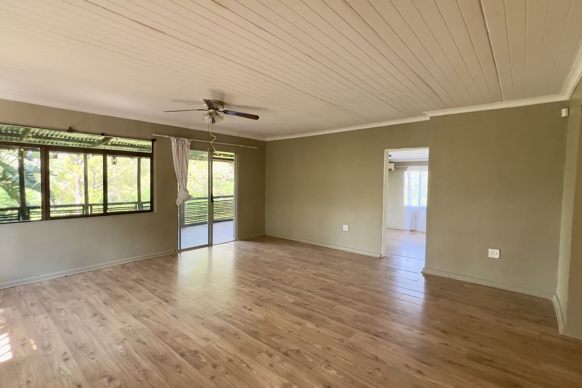 Spacious living area featuring wood-look laminate flooring, a ceiling fan, and large windows providing natural light and garden views.