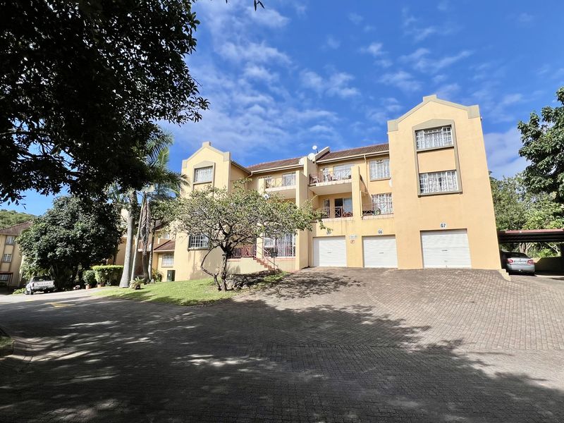 Front elevation of a multi-story apartment complex featuring a paved driveway, three integrated garages, and upper-level balconies.