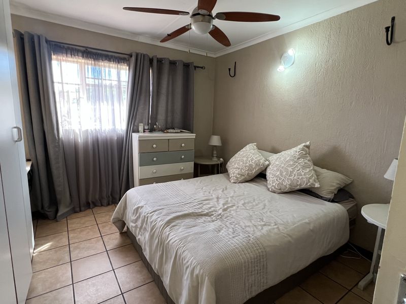 A functional bedroom featuring tiled flooring, a ceiling fan, and built-in wardrobe storage.