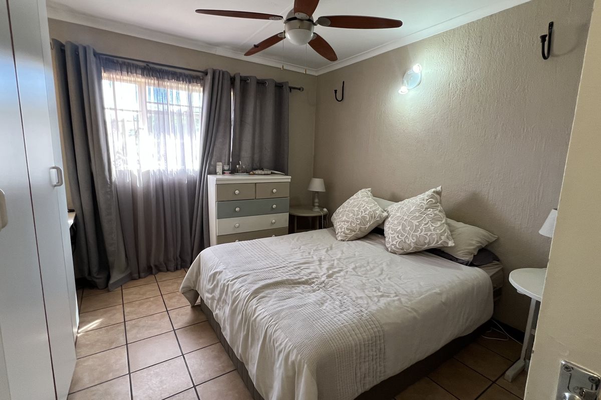A functional bedroom featuring tiled flooring, a ceiling fan, and built-in wardrobe storage.