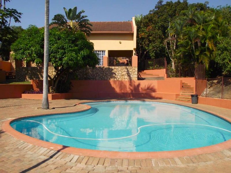 A well-maintained outdoor swimming pool area featuring brick paving, stone retaining walls, and landscaped surroundings with concrete stairs leading to the building.