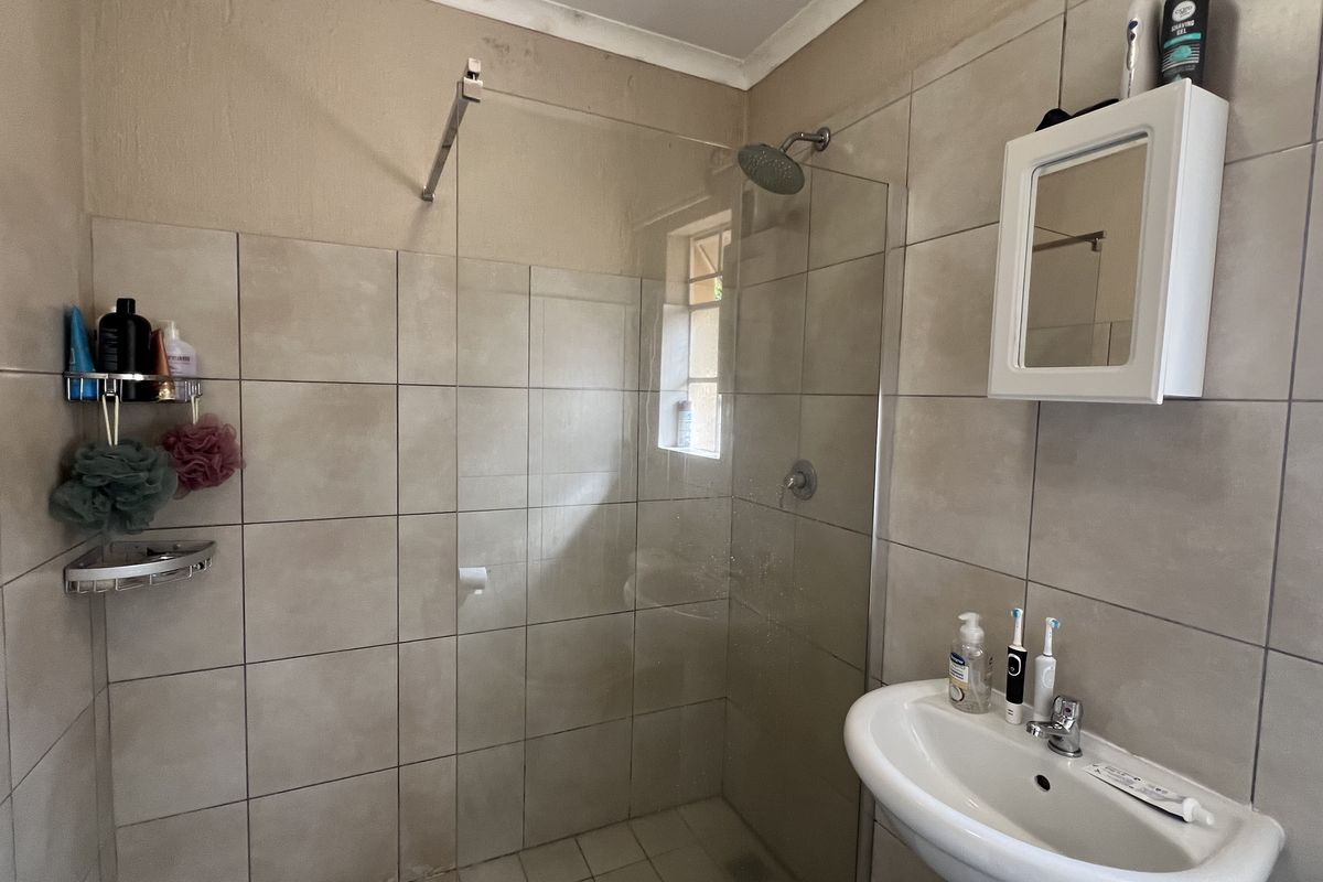 A functional bathroom featuring a glass-enclosed shower, pedestal basin, and wall-mounted vanity cabinet with neutral ceramic tiling.