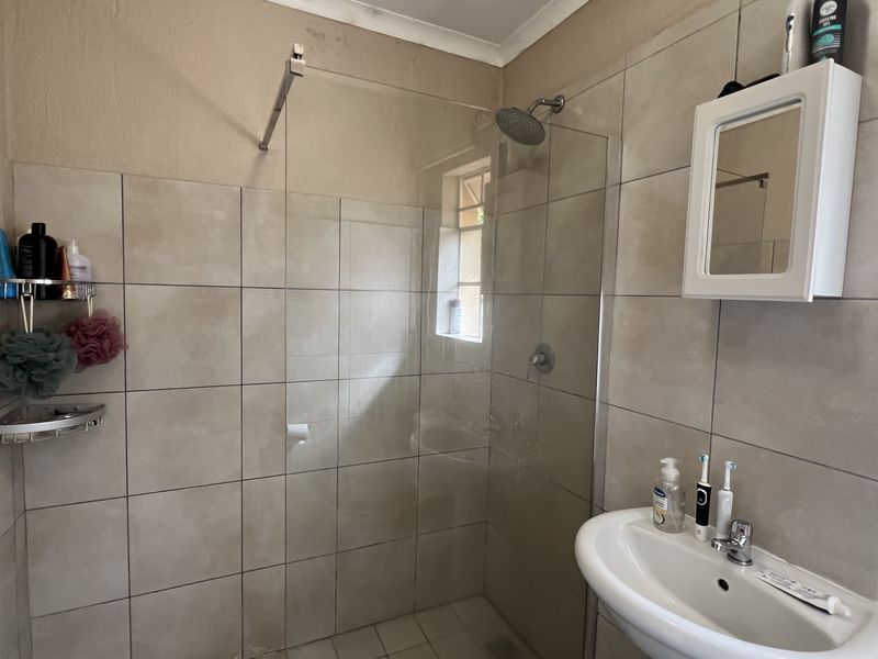 A functional bathroom featuring a glass-enclosed shower, pedestal basin, and wall-mounted vanity cabinet with neutral ceramic tiling.