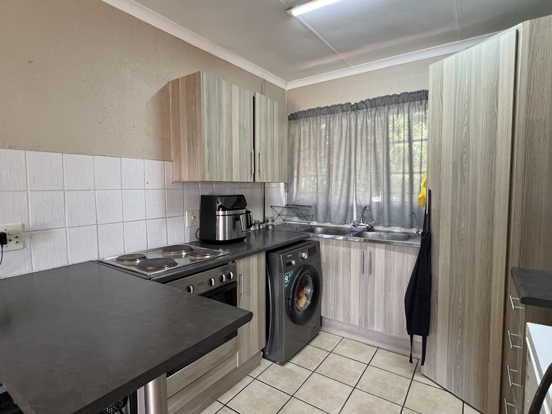 A functional kitchen featuring laminate cabinetry, a built-in electric stove, double stainless steel sink, and tiled backsplash with ceramic flooring.